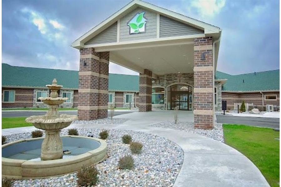 Community entrance with a stone fountain and brick porte-cochère under the Comfort Care logo