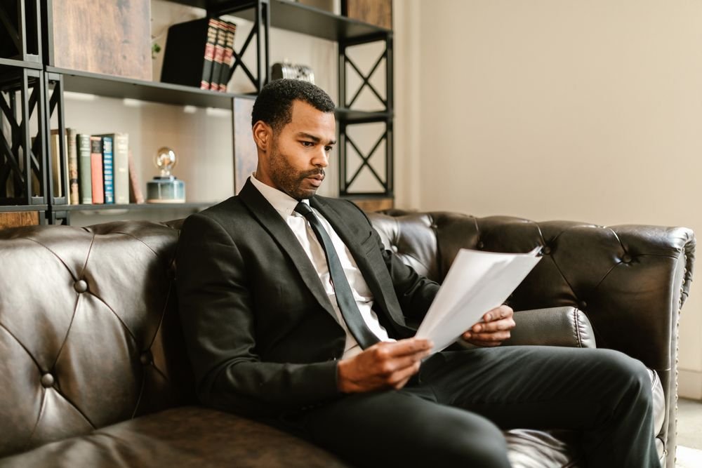 An owner in a suit reading a short report, relaxed on a leather sofa in a warm office