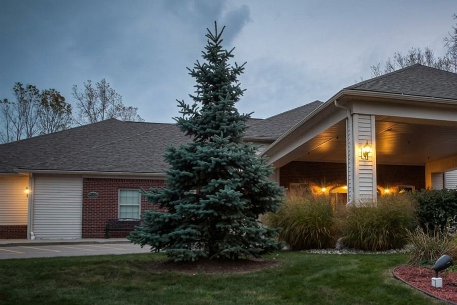 Lit entrance of an assisted living community at dusk, with a blue spruce in front