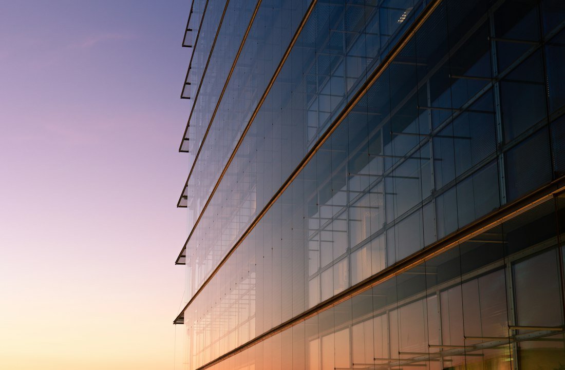 A modern glass office tower facade reflecting a dusk sky, representing institutional capital