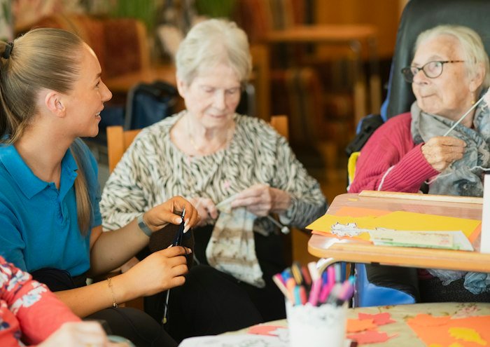 A caregiver helping residents with a knitting activity